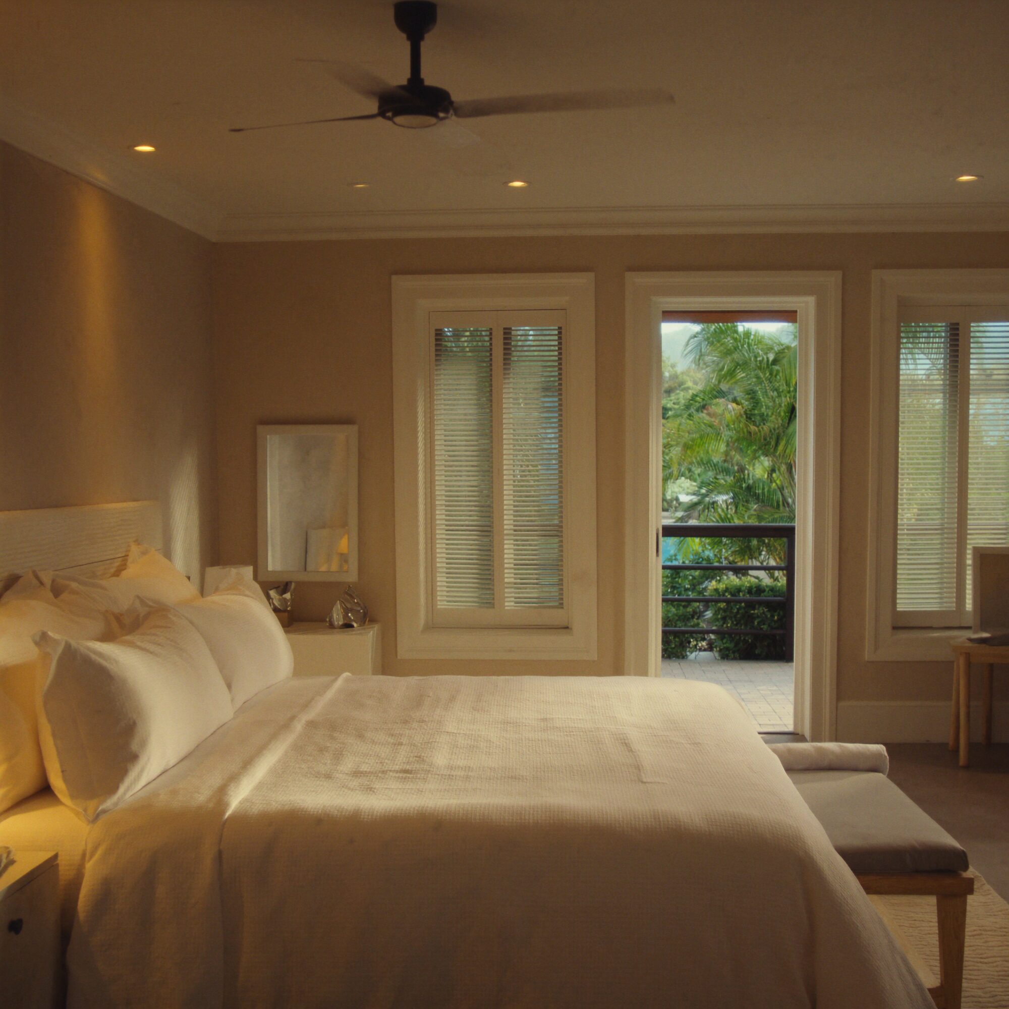 The villa's master bedroom with soft linen and louvred light, looking out over the canal