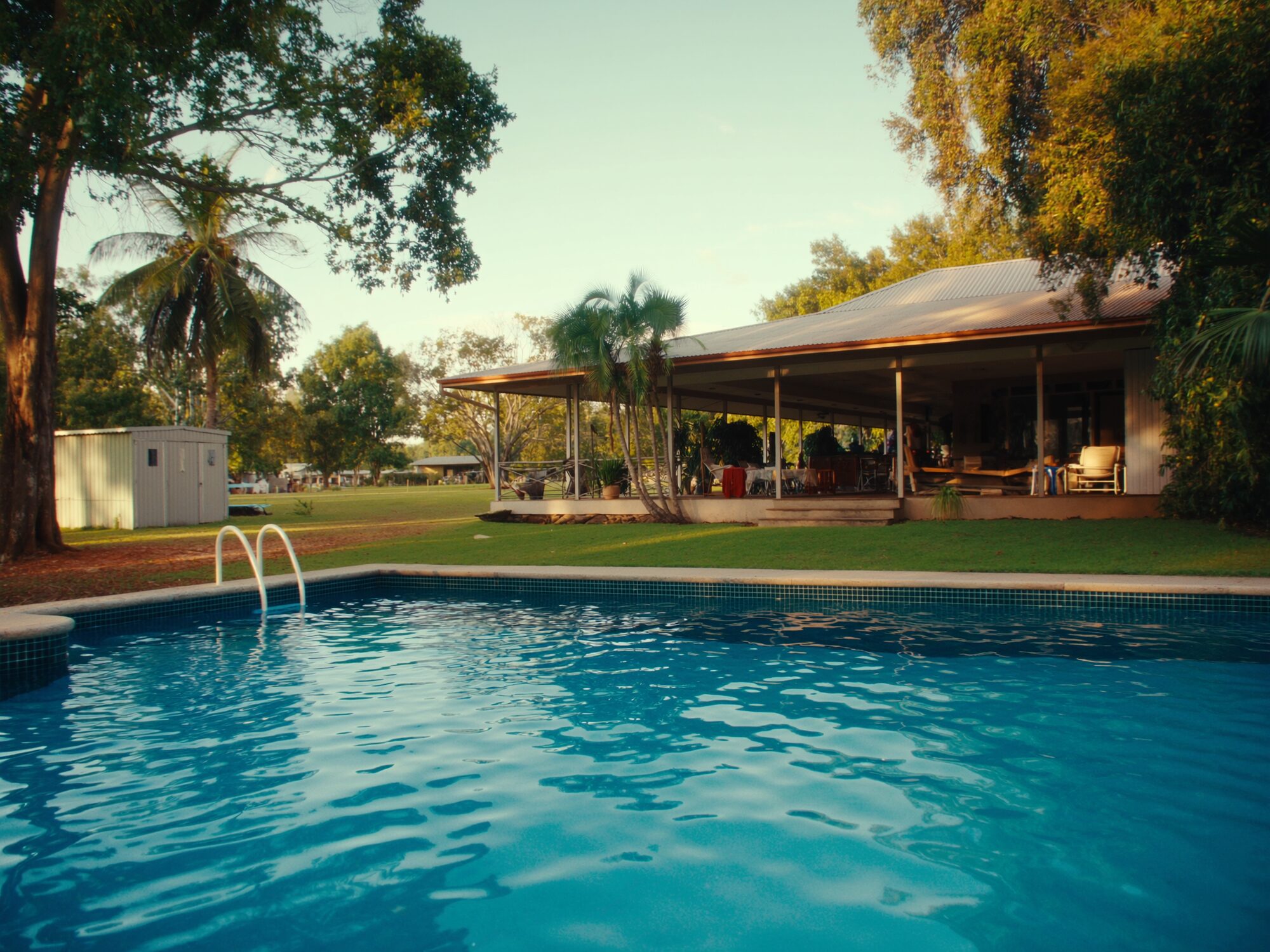 Sprawling Howard Springs acreage home with a large pool among palms and mango trees at golden hour